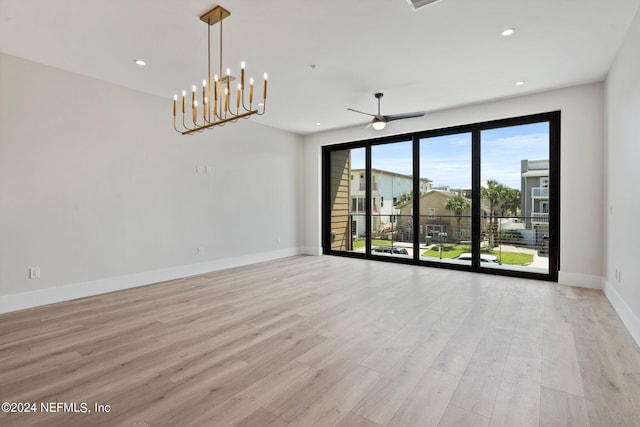 empty room with ceiling fan with notable chandelier and light hardwood / wood-style floors