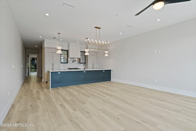 kitchen featuring ceiling fan with notable chandelier, pendant lighting, tasteful backsplash, a large island, and light hardwood / wood-style flooring