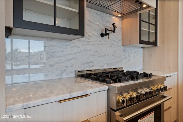 kitchen featuring high end stainless steel range oven, premium range hood, light brown cabinetry, and decorative backsplash