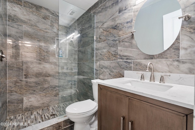 bathroom with vanity, toilet, tile walls, and a tile shower