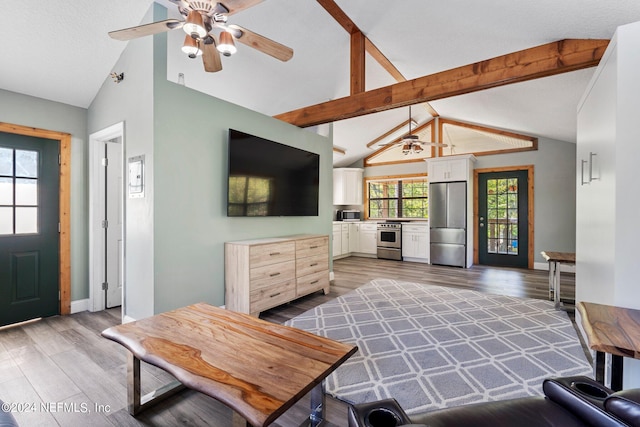 living room with ceiling fan, wood-type flooring, and vaulted ceiling with beams