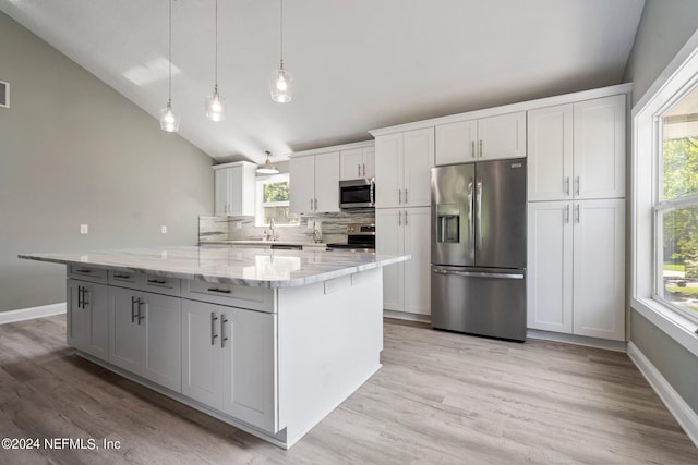 kitchen with appliances with stainless steel finishes, tasteful backsplash, lofted ceiling, white cabinets, and a center island