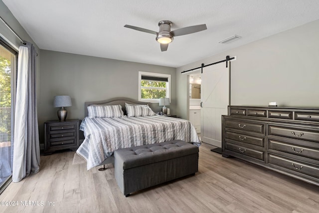 bedroom with ceiling fan, ensuite bath, a barn door, and light wood-type flooring