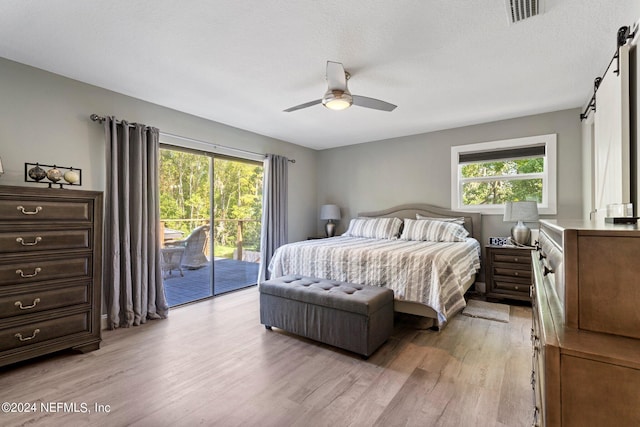 bedroom featuring access to outside, light wood-style flooring, a barn door, and visible vents