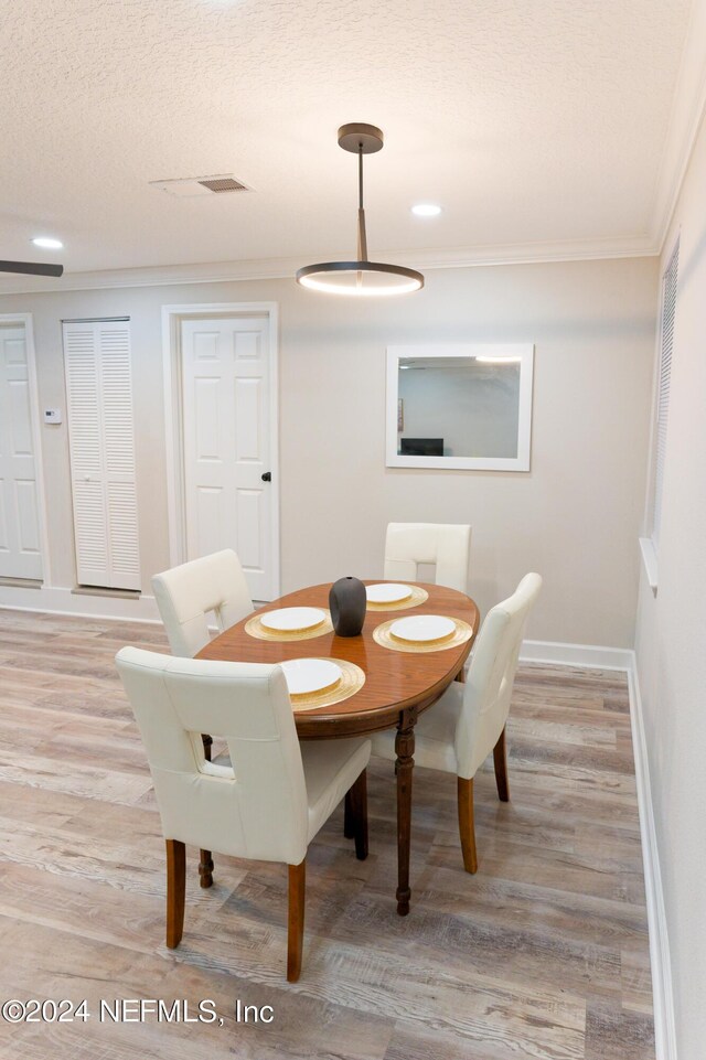 dining room featuring light wood-type flooring, a textured ceiling, and ornamental molding