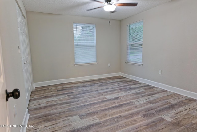 empty room with baseboards, a textured ceiling, wood finished floors, and a ceiling fan