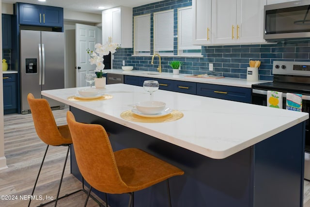 kitchen with blue cabinetry, light countertops, stainless steel appliances, decorative backsplash, and light wood-style flooring