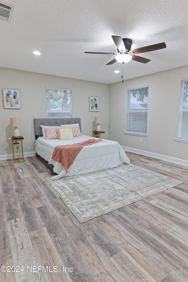 bedroom with a textured ceiling, visible vents, baseboards, wood finished floors, and a ceiling fan