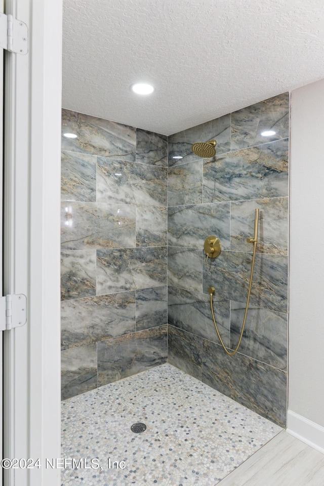 full bathroom with wood finished floors, baseboards, tiled shower, and a textured ceiling