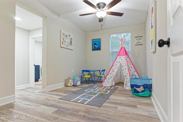 playroom with light hardwood / wood-style floors, ceiling fan, and a textured ceiling