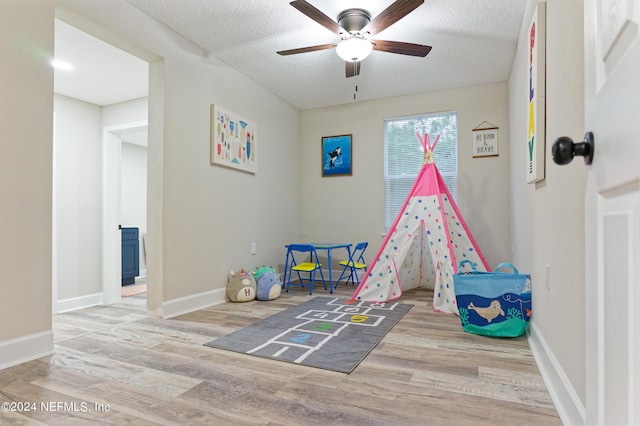 recreation room with baseboards, a textured ceiling, wood finished floors, and a ceiling fan