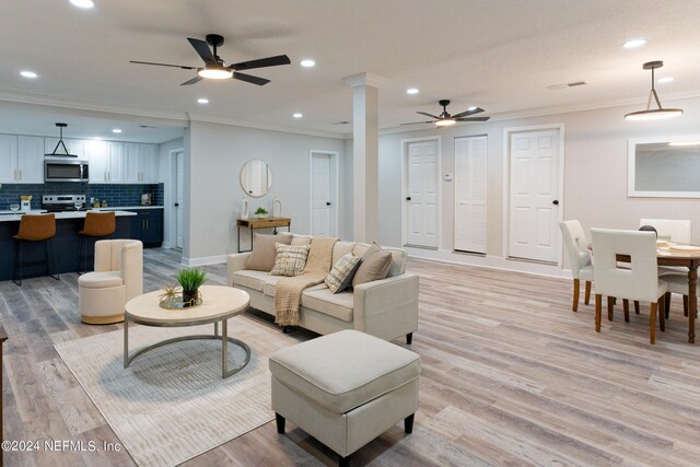 living room with ornamental molding, light wood-type flooring, ceiling fan, and decorative columns