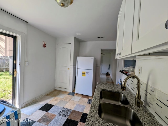 kitchen with dark stone countertops, white cabinetry, sink, and white fridge