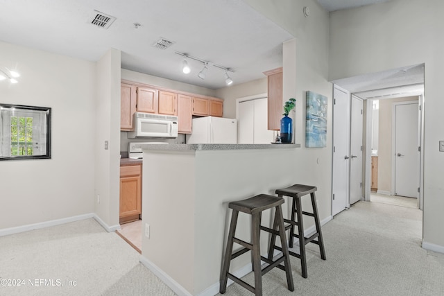 kitchen with kitchen peninsula, white appliances, light brown cabinets, and a breakfast bar