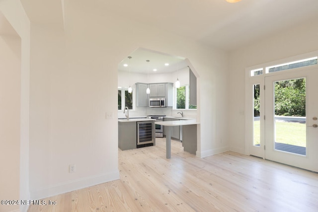 kitchen with hanging light fixtures, stainless steel appliances, beverage cooler, light hardwood / wood-style flooring, and sink