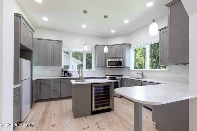 kitchen featuring wine cooler, decorative light fixtures, gray cabinets, appliances with stainless steel finishes, and light wood-type flooring