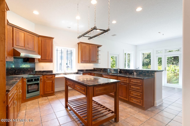 kitchen with dark stone countertops, light tile patterned floors, stainless steel oven, and kitchen peninsula