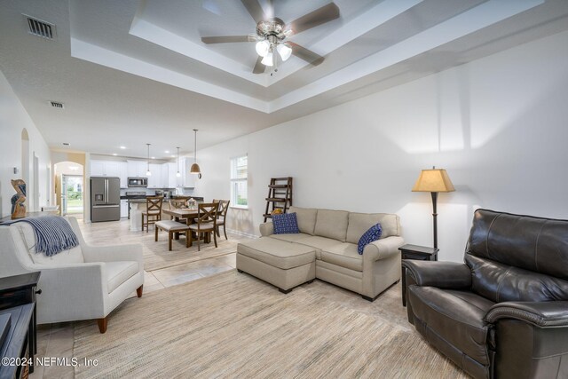 tiled living room with a raised ceiling, ceiling fan, and plenty of natural light