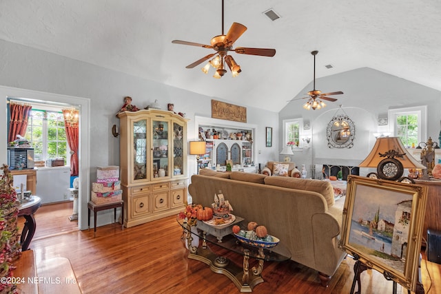 living room with ceiling fan, a textured ceiling, light hardwood / wood-style flooring, a fireplace, and vaulted ceiling