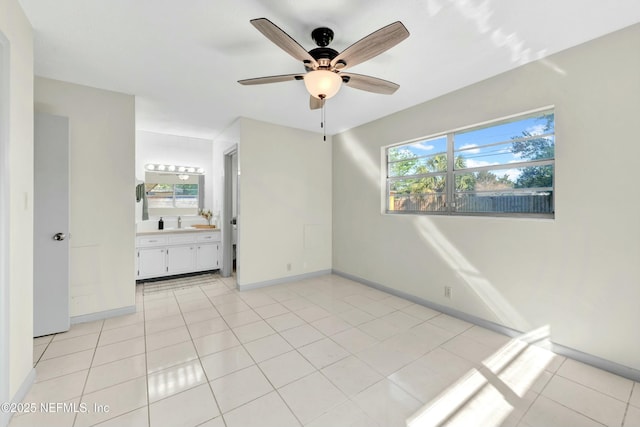 unfurnished bedroom with light tile patterned floors, connected bathroom, baseboards, and a sink