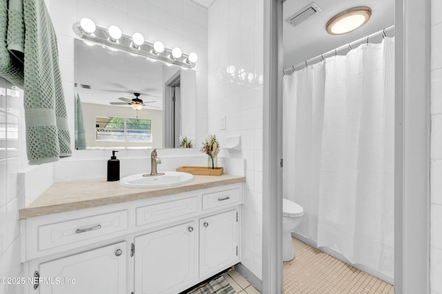 bathroom with tile patterned flooring, toilet, vanity, tile walls, and a ceiling fan