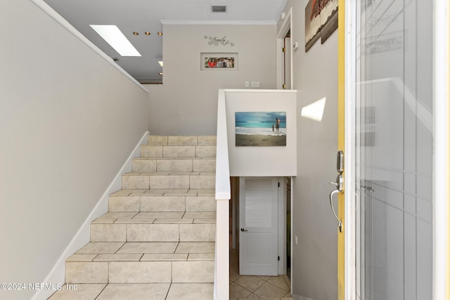 staircase with a skylight, crown molding, and tile patterned flooring