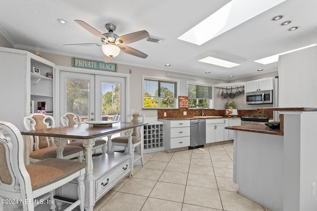 kitchen with appliances with stainless steel finishes, white cabinetry, ceiling fan, french doors, and ornamental molding