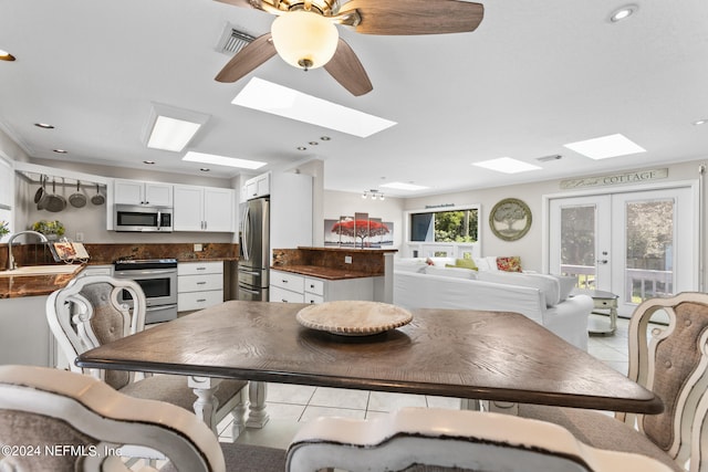 tiled dining space featuring sink, a skylight, ornamental molding, ceiling fan, and french doors