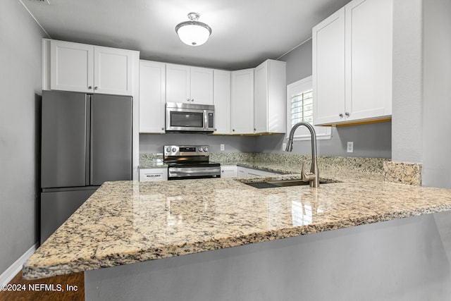 kitchen with light stone counters, stainless steel appliances, sink, kitchen peninsula, and white cabinetry