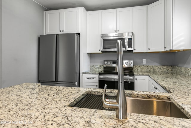 kitchen with appliances with stainless steel finishes, light stone counters, and white cabinetry