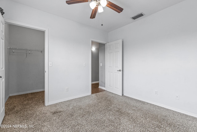 unfurnished bedroom featuring ceiling fan, a closet, dark colored carpet, and a spacious closet