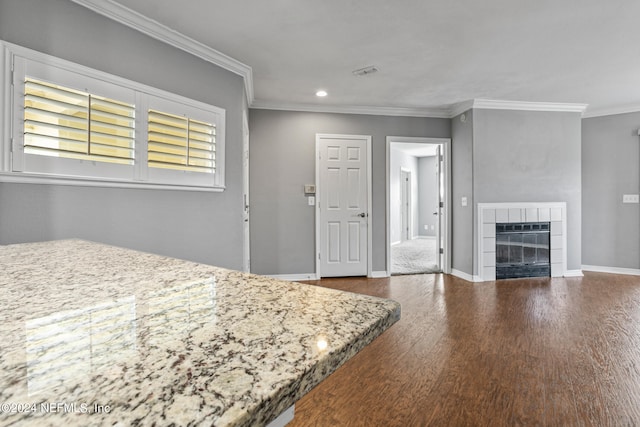 unfurnished bedroom featuring crown molding, a tiled fireplace, and hardwood / wood-style floors