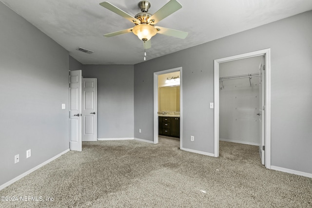 unfurnished bedroom featuring ceiling fan, connected bathroom, light carpet, and a walk in closet