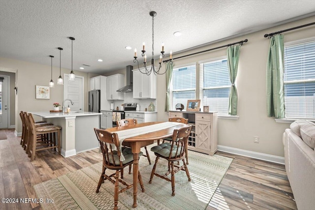 dining area featuring light hardwood / wood-style floors, sink, a textured ceiling, and an inviting chandelier