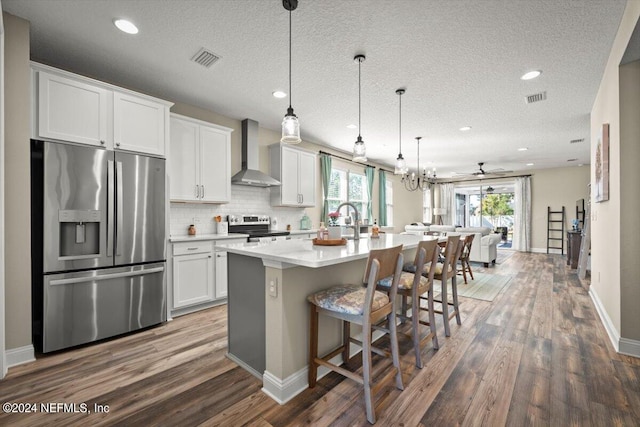 kitchen featuring white cabinetry, a center island with sink, wall chimney exhaust hood, and appliances with stainless steel finishes