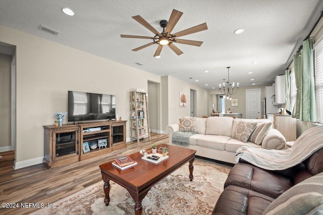 living room with hardwood / wood-style flooring, ceiling fan with notable chandelier, and a textured ceiling