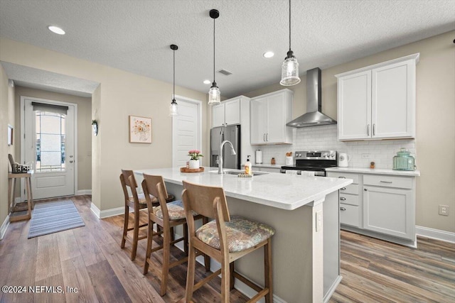 kitchen featuring appliances with stainless steel finishes, wall chimney range hood, dark hardwood / wood-style floors, white cabinetry, and an island with sink