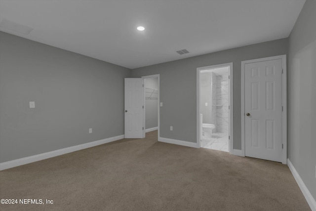 unfurnished bedroom featuring light carpet, ensuite bath, a closet, and a walk in closet