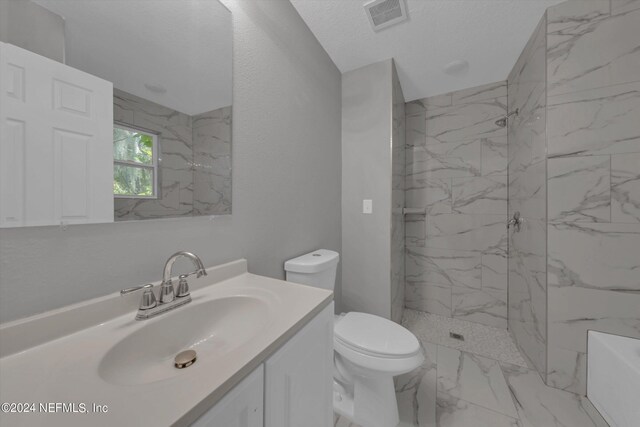 bathroom with a textured ceiling, a tile shower, vanity, and toilet