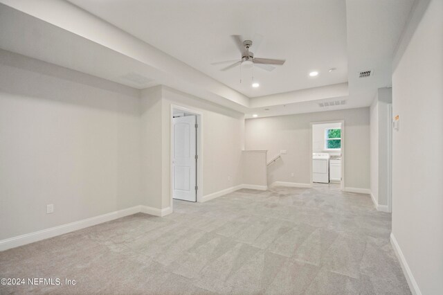 unfurnished room featuring light carpet, ceiling fan, a raised ceiling, and washer and clothes dryer