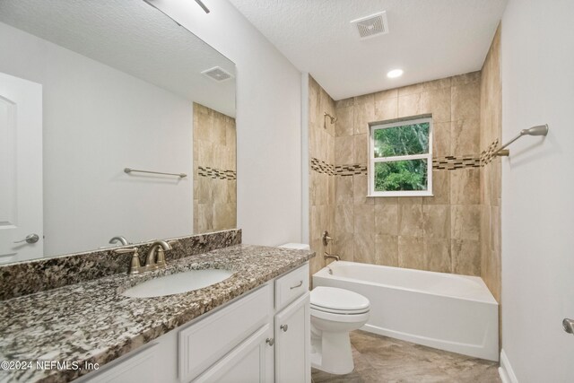 full bathroom featuring a textured ceiling, tiled shower / bath combo, vanity, and toilet