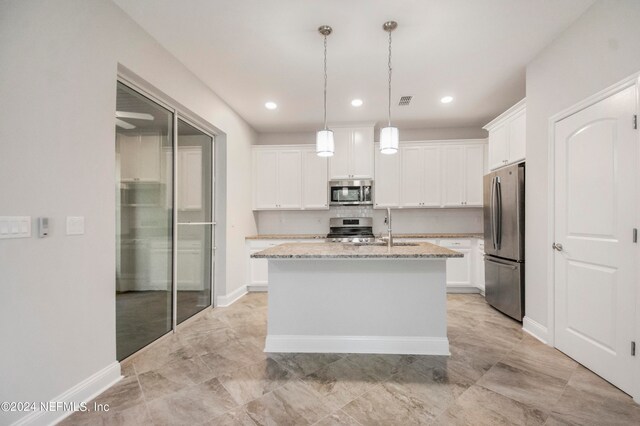 kitchen with light stone counters, an island with sink, hanging light fixtures, white cabinetry, and appliances with stainless steel finishes