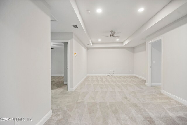 empty room featuring ceiling fan, a raised ceiling, and light carpet