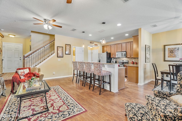 kitchen featuring a textured ceiling, a kitchen island, stainless steel appliances, decorative light fixtures, and ceiling fan