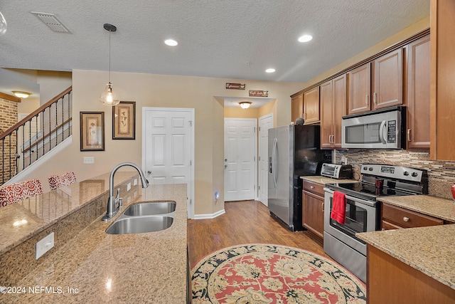 kitchen featuring light stone counters, sink, decorative light fixtures, stainless steel appliances, and light wood-type flooring