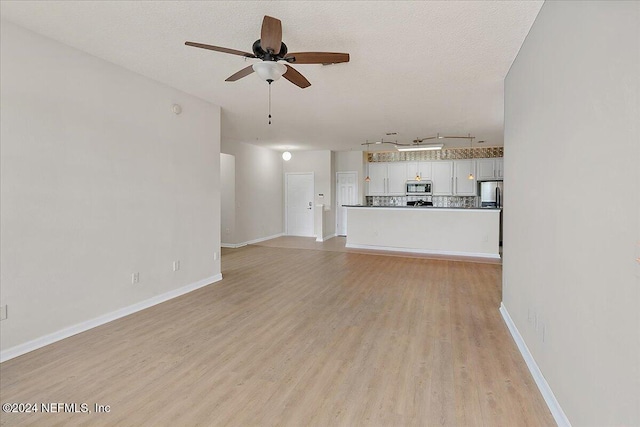 unfurnished living room featuring light wood-type flooring, a textured ceiling, track lighting, and ceiling fan