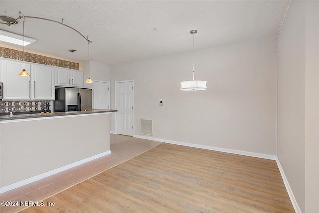 kitchen with light wood-type flooring, white cabinetry, stainless steel refrigerator with ice dispenser, and tasteful backsplash