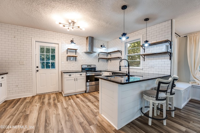 kitchen with white cabinets, stainless steel range with electric stovetop, light wood-type flooring, sink, and wall chimney range hood