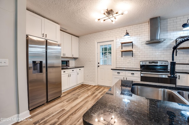 kitchen featuring a textured ceiling, wall chimney range hood, white cabinetry, appliances with stainless steel finishes, and light hardwood / wood-style floors