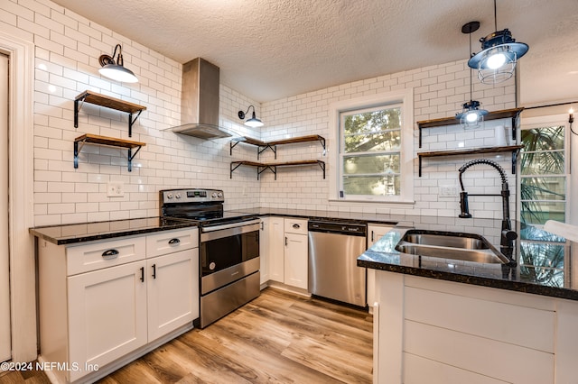 kitchen featuring hanging light fixtures, light hardwood / wood-style floors, white cabinetry, wall chimney exhaust hood, and stainless steel appliances